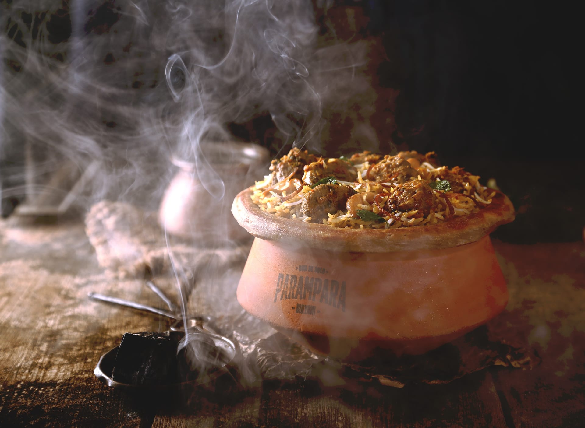 Hyderabadi mutton dum biryani in earthen handi, smoke rising — Parampara Biryani, Pune